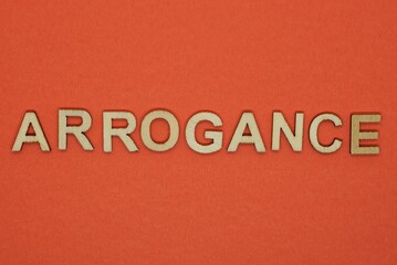 text the word arrogance from gray wooden small letters on an red table