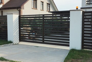 one closed black wooden gate and part of a fence wall made of white concrete pillars and planks...