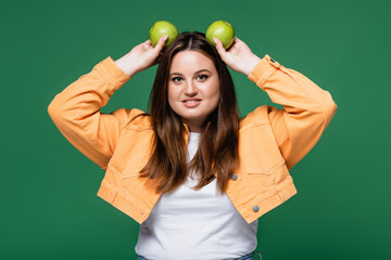 Positive plus size woman holding apples above head isolated on green