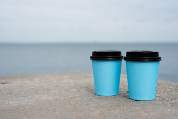 Obraz premium Two coffee cups on the ground close up on the sea water background.