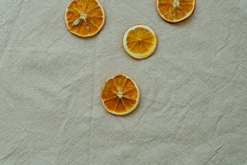 Vier getrocknete Orangenscheiben auf einem beigen Leinen Tischtuch. Flat lay, minimalistisch.