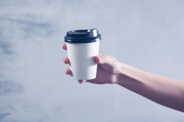 a female hand holds a disposable cup of coffee