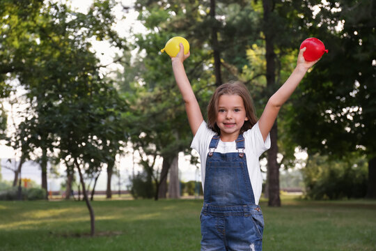 Cute little girl holding water bombs in park - Powered by Adobe