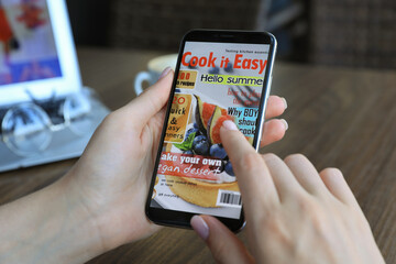 Woman reading online magazine on mobile phone at wooden table, closeup