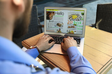 Man reading online magazine on laptop at wooden table, closeup
