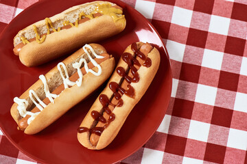 Top view of tasty hot dogs with mustard and ketchup on a plate over red checkered plaid napkin