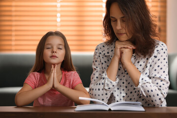 Mature woman with her little granddaughter praying together over Bible at home