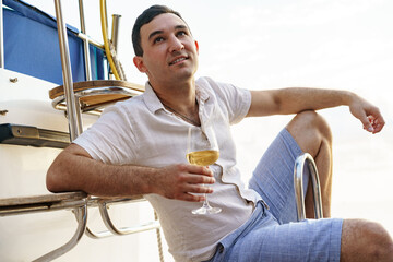 Young man holding a glass of wine on an open deck of a cruise boat