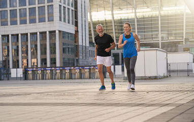 Active middle aged couple, man and woman running together in the city while training outdoors
