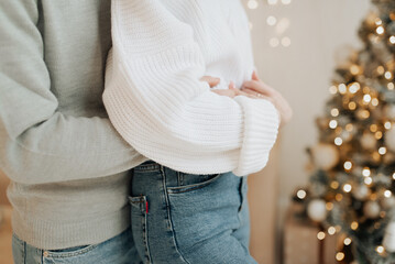 man and girl in sweaters and blue jeans hugging on the background of the Christmas tree