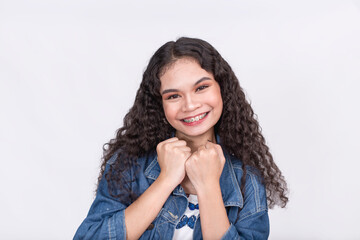 A cute asian teenage lady with long curly hair makes a cute and reserved success gesture. Against a...