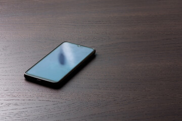 Black smartphone turned off lies on a dark wooden table