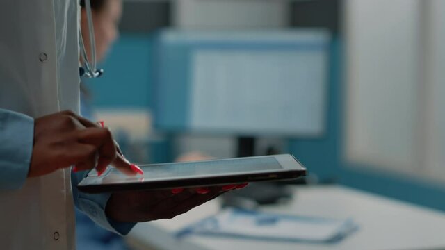 Close up of african american doctor using digital tablet with hands on touch screen for checkup. Black medic holding device with internet and information for medical practice and care