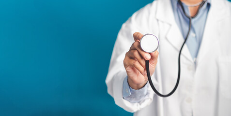 Hand of a doctor holding a stethoscope while standing on a blue background. Close-up photo. Space for text. Medical, treatment, and healthcare concept