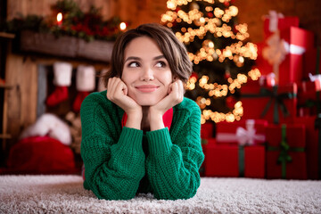 Photo of excited dreamy young woman dressed knitted sweater sitting arms cheeks smiling indoors room home house