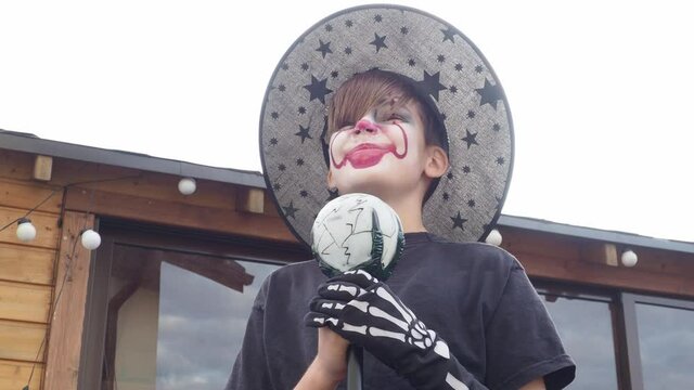 boy with Halloween costume, scary jocker or clown makeup holding wand outdoor. Horror concept of party