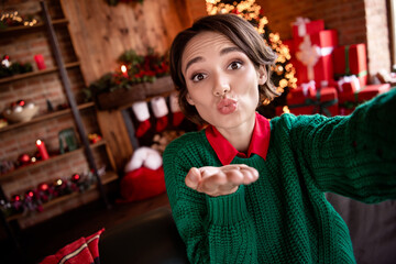 Photo of charming flirty young woman dressed green sweater recording self video sending you arm kiss indoors house home room