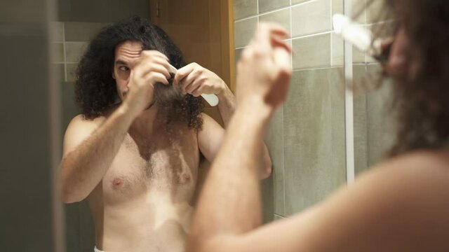 Young adult combing afro hair with white comb in the mirror shirtless