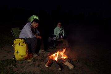 Couple sitting near bonfire in camp at night