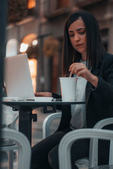 Mujer joven empresaria moviendo su café en una cafeteria mientras trabaja con su ordenador laptop 