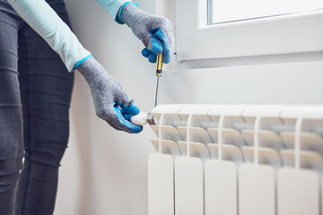 Handyman with gloves fixing and bleeding air from central heating gas radiator system at home.