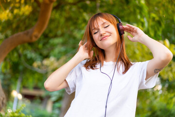Young pretty redhead woman at outdoors listening music