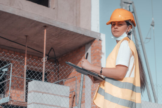 Arquitecta de obra estudiando el perimetro del edificio para su construcci&oacute;n junto con otros empleados de obra asegurados con sus cascos de protecci&oacute;n mientras se planifica la maquetaci&oacute;n