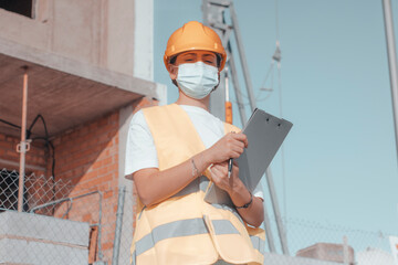 Mujer joven arquitecta con mascarilla quirúrgica trabajando en la obra en una construcción de un...
