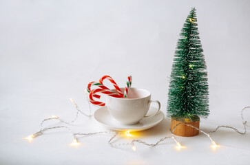 a cup with a saucer and caramel canes and a small artificial Christmas tree on a white background with a place for text