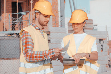 Mujer y Hombre arquitectos de una constructora para una inmobiliaria trabajando en equipo con cascos mientras revisan los planos de la construcción de obra