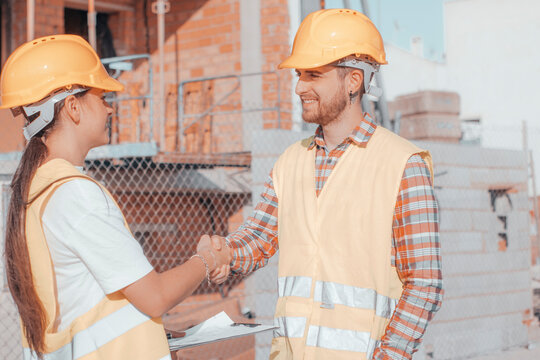Muchachos j&oacute;venes de ingenier&iacute;a sonriendo en la obra de un edificio estrech&aacute;ndose la mano para conocerse y trabajar en equipo en la reforma y construcci&oacute;n de la estructura