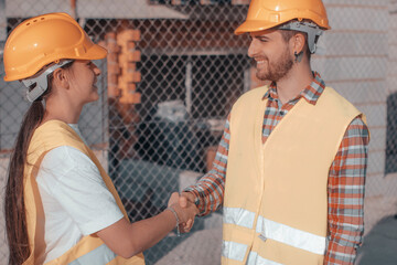 Equipo de jóvenes de ingeniería sonriendo en la obra de un edificio estrechando la mano para...