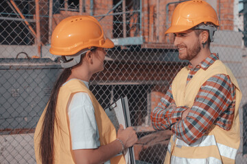 Equipo de ingenieros sonrientes comunicándose y charlando sobre la construcción del edificio junto con materiales de obra y cascos de seguridad