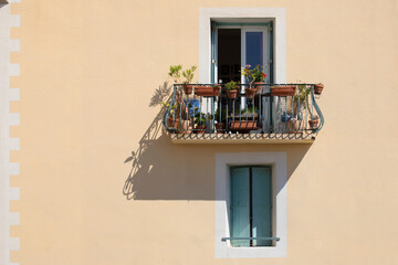 Fenêtre d'un immeuble dans une ville du Sud de la France à la façade colorée et au balcon fleuri, en été sous le soleil de midi qui projette les ombres des reliefs. Ville de Sète