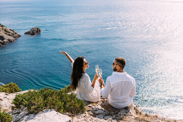 A couple in love celebrates their engagement on the seashore. A beautiful couple drinks champagne by the sea. Honeymoon trip. Lovers on the beach. Wedding travel. Couple on vacation. Copy space