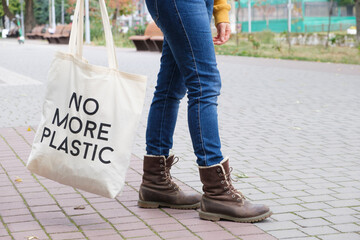 Human feet in boots and a reusable cloth bag with the inscription No more plastic