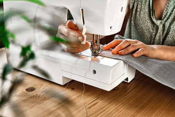 Seamstress sewing the linen fabric on the sewing machine in small studio. Fashion atelier,...