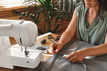 Woman taking measurements on the linen fabric. Seamstress sewing on the sewing machine in small...