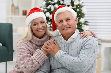 Fototapeta premium Happy mature couple in Santa hats at home. Christmas celebration