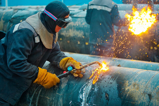 Svrshchiki cut with acetylene welding old pipes of the gas pipeline of large diameter. Utilization of metal pipes for gasification. Work outdoors during the day.