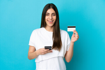 Young caucasian woman isolated on blue background buying with the mobile with a credit card