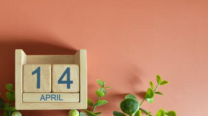 April 14, Date design with calendar cube and leaf on orange background.