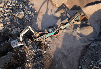 Excavator at landfill the load concrete waste in a mobile jaw crusher machine. Disposal of construction waste. Recycling concrete and asphalt from demolition. Re-use concrete after demolition.