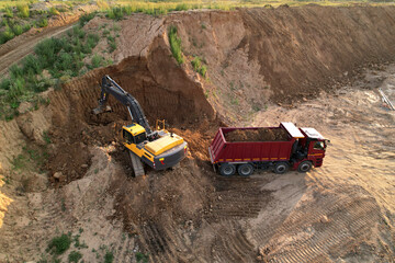 Excavator load the sand into dump truck. Loader digging ground for foundation pit. Earthmoving at construction site. Aerial view of an backhoe on earthworks. Open pit development and mining.