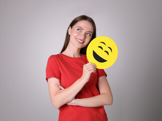Happy young woman with laughing emoji on grey background
