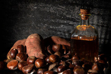 Raw sweet potatoes and chestnuts with muscat bottle on dark background.