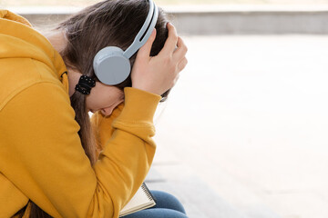 Sad teenage girl in headphones will cover her face with her hands, a place for text