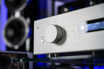 Stereo amplifier against the background of a home speaker system. Close control knob, silver metal body. Listen to your favorite music at home loudly. Create a holiday mood. An audiophile's dwelling.