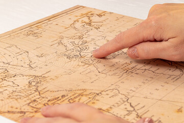 female hand shows the place of travel on the world map on the background of a white wooden table. close-up. selective focus