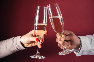 Male and female hands holding and clinking champagne glasses with champagne on burgundy background